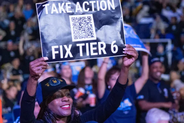 Union member holdin a sign that says "take action, fix tier 6" with a qr code